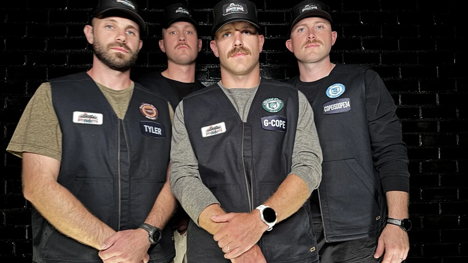 The four Hunters lined up in front of a black brick wall